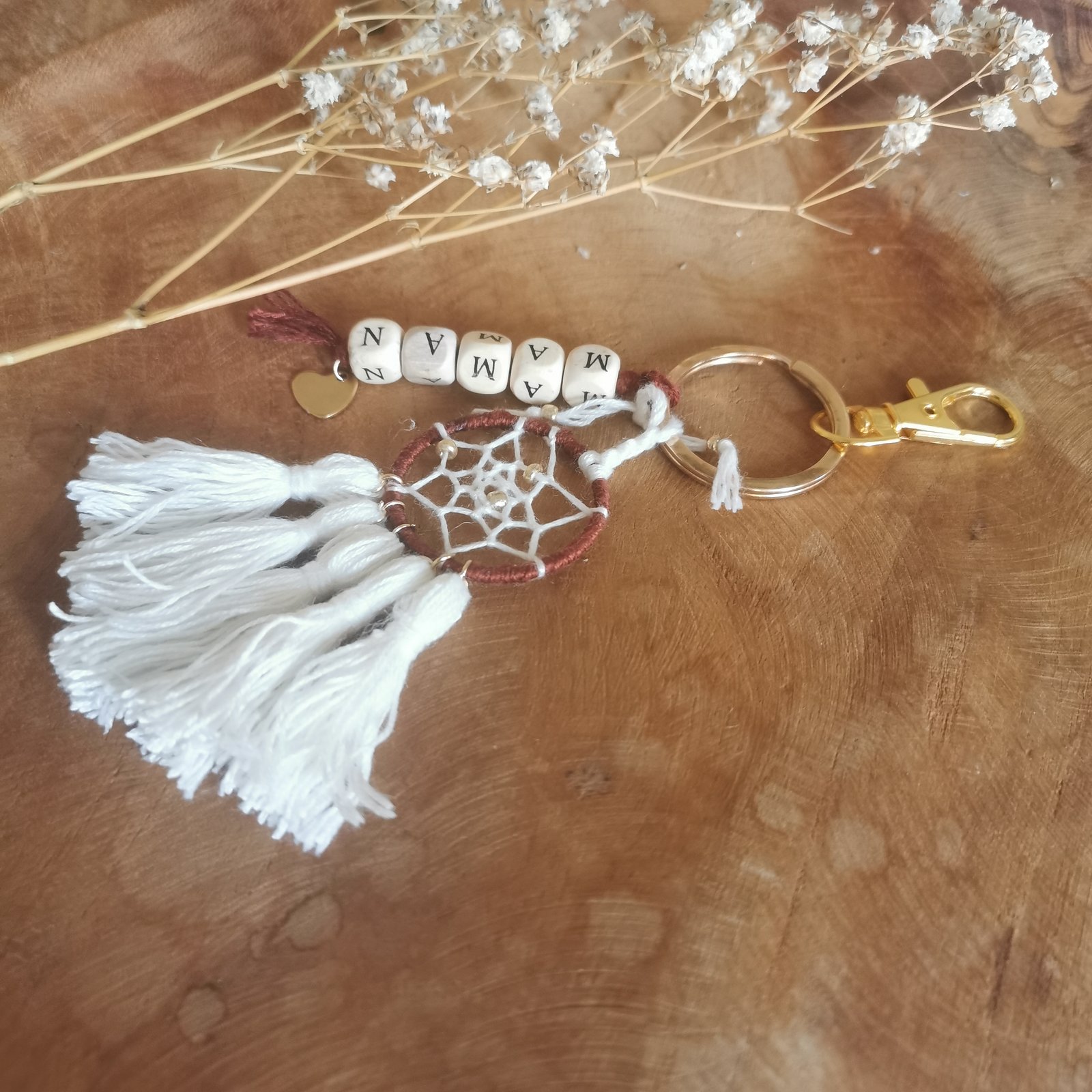 Petit attrape-rêves blanc artisanal en porte-clés, avec pompons et perles lettres en bois.