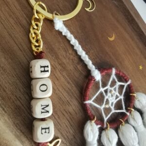 Porte-clé Votum Compagnon Nomade avec perles en bois mot HOME et pompons blancs.