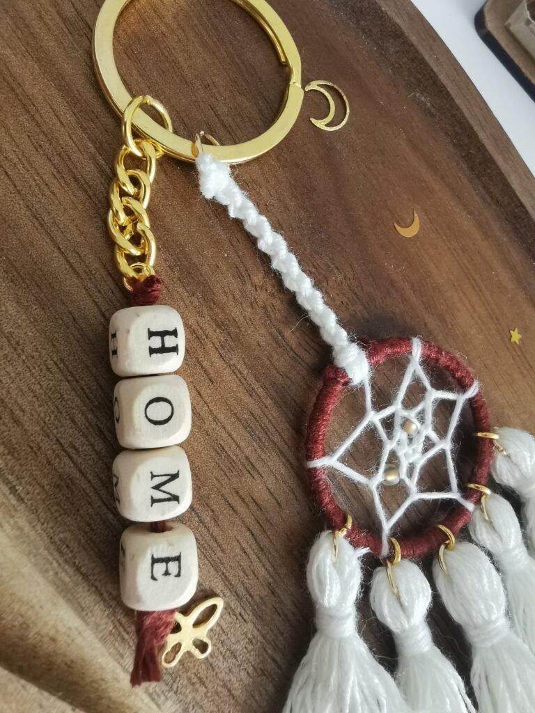 Porte-clé Votum Compagnon Nomade avec perles en bois mot HOME et pompons blancs.