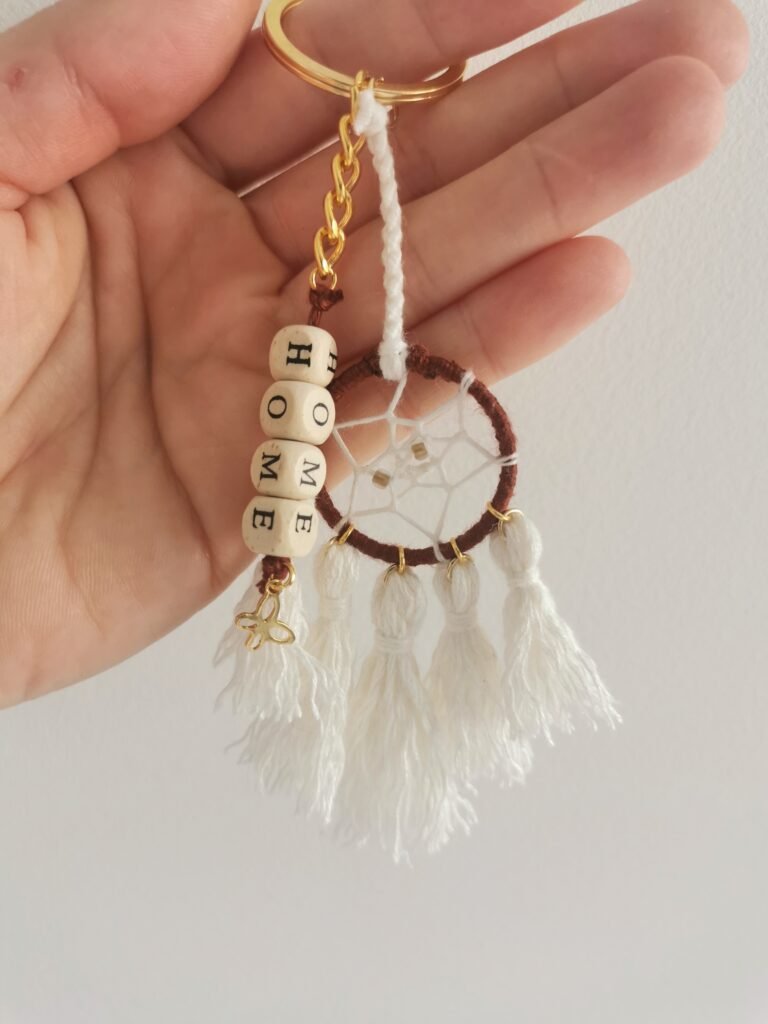 Porte-clé Votum Compagnon Nomade avec perles en bois mot HOME et pompons blancs.