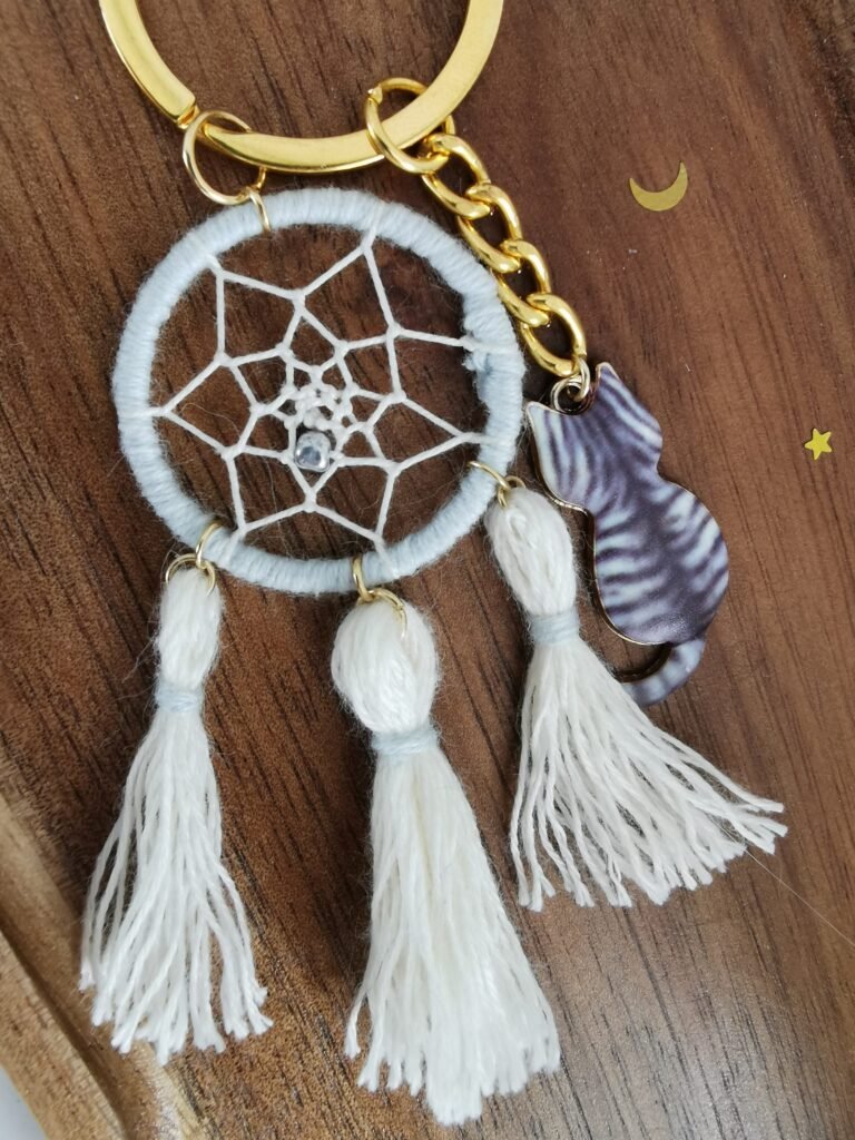 Porte-clés Felis Prospicio sur bois : mini attrape-rêve blanc, pompons et breloque chat tigré gris.