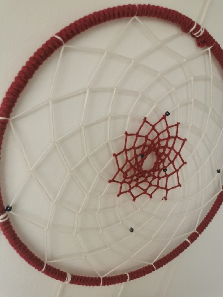 Gros plan sur le tissage artisanal en forme d'étoile rouge cerise d'un attrape-rêves fait main.
