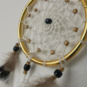 Détail de l'attrape-rêves chic "Zéphyr" montrant le tissage artisanal ivoire et les perles dorées.