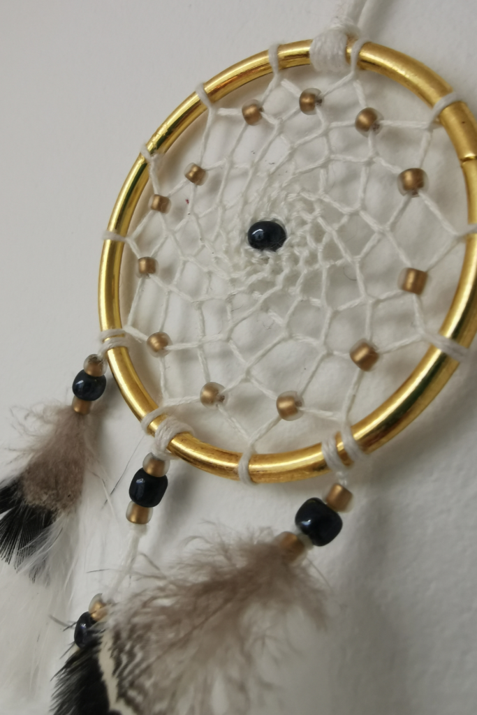 Détail de l'attrape-rêves chic "Zéphyr" montrant le tissage artisanal ivoire et les perles dorées.